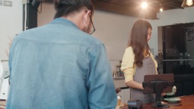 Genç Asyalı bayan barista elinde kahve fincanı tutarak kendini mutlu hissediyor ve kafe restoranındaki barın arkasında tüketiciye sıcak kahve servisi yapıyor. Küçük işletme, yiyecek ve içecek, hizmet zihin konsepti.