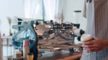Kafe restoranındaki tezgahın arkasında duran tüketiciye sıcak kahve bardağı servisi yapan genç Asya 'lı erkek barista. Küçük işletme, yiyecek ve içecek, hizmet zihin konsepti.