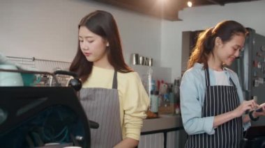 Cep telefonu ve dijital tabletle sipariş alan genç Asyalı bayan barmen, kafe restoranında cep telefonuyla müşteriyle konuşurken tezgahın arkasında duruyor. Sahip küçük işletme kavramı.