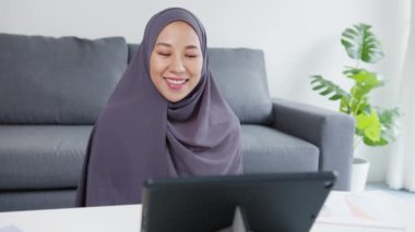 Asyalı Müslüman kadın, evde çalışırken konferans görüntülü konuşmasında meslektaşlarına satıştan bahsederken türban takıyor. Corona virüsü için sosyal uzaklık, karantina.