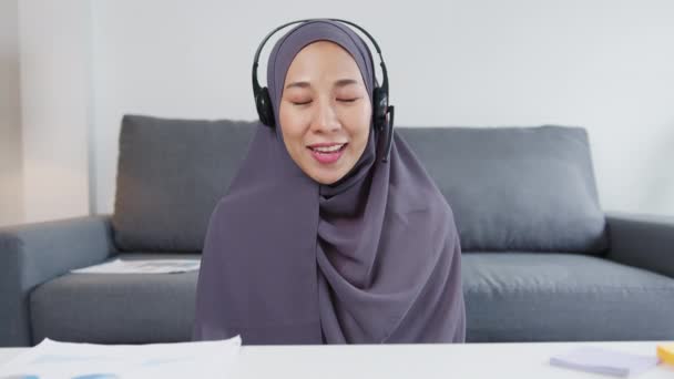アジアのイスラム教徒の女性は 自宅のリビングルームでリモートワーク中にビデオ通話で販売報告書について同僚にコンピュータのラップトップトークを使用してヘッドフォンを着用します 社会的距離コロナウイルスの隔離 — ストック動画