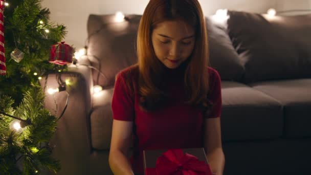 年轻的亚洲女性在家里的客厅里 在圣诞树旁的礼物盒里摆满了装饰品 开开开心心 平安夜快乐新年佳节快乐 — 图库视频影像