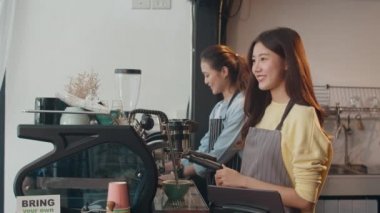 Genç Asyalı kadınlar kafedeki tabletle cep telefonu kullanırlar. Kahveci kız kahve dükkanındaki bardaki müşteriden emir alıyor. Sahip küçük işletme kavramı.