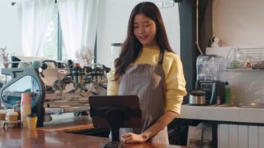 Genç Asyalı kadın self-servis kafe restoranındaki tabletle bağlantı kurulamayan cep telefonu kullanıyor. Kahveci kız kahve dükkanındaki bardaki müşteriden emir alıyor. Küçük işletme sahibi.