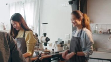 Kafe restoranındaki tezgahın arkasında duran tüketiciye sıcak kahve bardağı servis eden genç Asyalı bayan barista. Küçük işletme, yiyecek ve içecek, hizmet zihin konsepti.