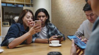 Bir grup mutlu Asyalı genç arkadaş birlikte kafeteryada otururken güzel vakit geçiriyorlar ve birlikte akıllı telefon kullanıyorlar. Kahve dükkanı tatil aktivitesi, modern arkadaşlık yaşam tarzı konsepti..
