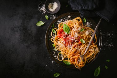 Domates soslu lezzetli iştah açıcı klasik İtalyan spagetti makarna peynir parmesan ve fesleğen plaka karanlık tablo üzerinde. Yukarıdan görünüm, üstten görünüm