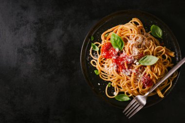 Domates soslu lezzetli iştah açıcı klasik İtalyan spagetti makarna peynir parmesan ve fesleğen plaka karanlık tablo üzerinde. Yukarıdan, yatay görüntüleme