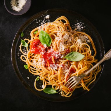 Domates soslu lezzetli iştah açıcı klasik İtalyan spagetti makarna peynir parmesan ve fesleğen plaka karanlık tablo üzerinde. Yukarıdan görünüm, kare kırpma