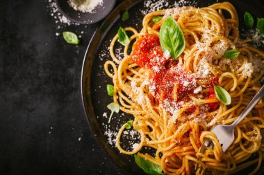 Domates soslu lezzetli iştah açıcı klasik İtalyan spagetti makarna peynir parmesan ve fesleğen plaka karanlık tablo üzerinde. Yukarıdan görünüm, üstten görünüm