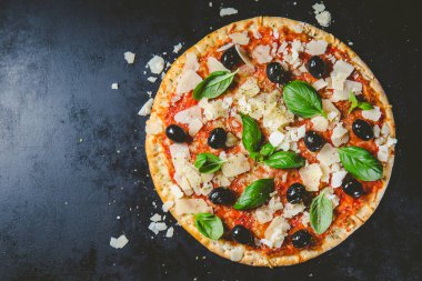 Koyu siyah masada lezzetli iştah açıcı klasik İtalyan geleneksel pizza peynir, zeytin, fesleğen ve taze sebze ile üstten görünüm. 