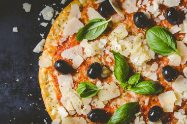Koyu siyah masada lezzetli iştah açıcı klasik İtalyan geleneksel pizza peynir, zeytin, fesleğen ve taze sebze ile üstten görünüm. 