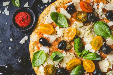 Koyu siyah masada lezzetli iştah açıcı klasik İtalyan geleneksel pizza peynir, zeytin, fesleğen ve taze sebze ile üstten görünüm. 