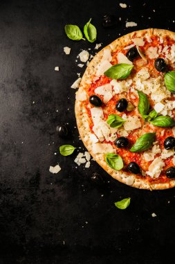 Koyu siyah masada lezzetli iştah açıcı klasik İtalyan geleneksel pizza peynir, zeytin, fesleğen ve taze sebze ile üstten görünüm. 
