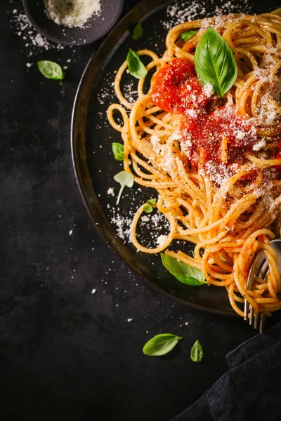 Domates soslu lezzetli iştah açıcı klasik İtalyan spagetti makarna peynir parmesan ve fesleğen plaka karanlık tablo üzerinde. Yukarıdan görünüm, üstten görünüm