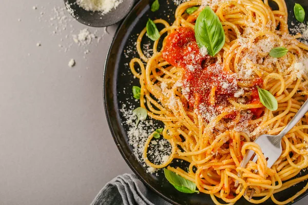 Domates soslu lezzetli iştah açıcı klasik İtalyan spagetti makarna peynir parmesan ve fesleğen plaka gri tablo üzerinde. Yukarıdan görünüm, üstten görünüm