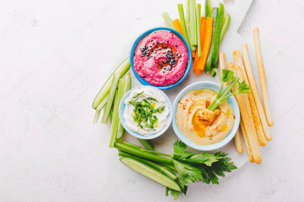 Appetizing vegetarian healthy dips sauces in small bowls with cut vegetables on cutting board. View from above. Healthy detox weight loss concept. 