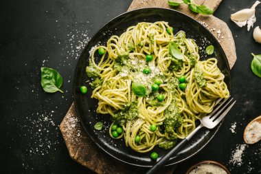 Lezzetli iştah açıcı makarna spagetti taze sosu pesto, yeşil bezelye ve peynir ile siyah tablo tabakta servis. Yukarıdan görüntüleyin. Yemeye hazır. Yatay