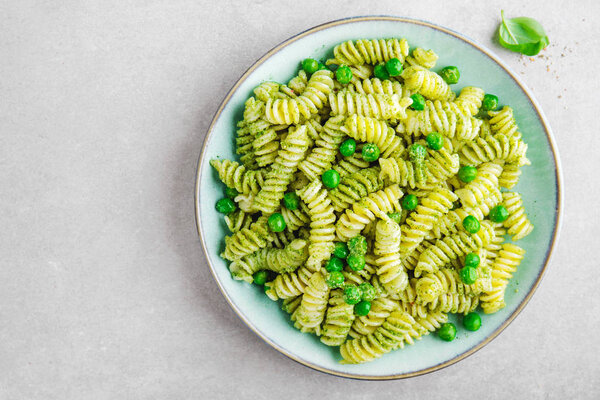 top view of italian pasta al bronzo with pesto sauce, green pea, basil and cheese served on grey tabletop