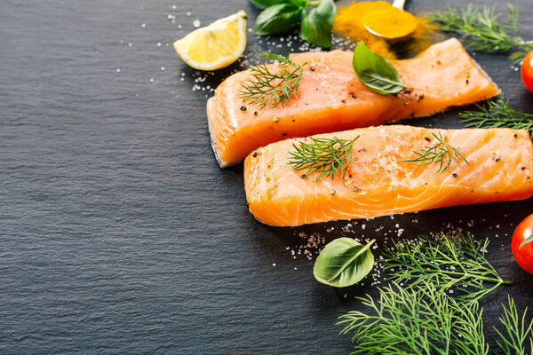 Raw fresh tasty salmon steaks on black table with ingredients