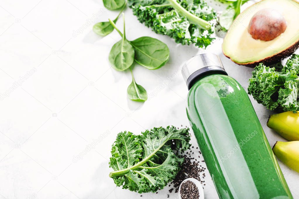 close-up shot of green smoothie in bottle with lettuce, avocado and bananas on white table