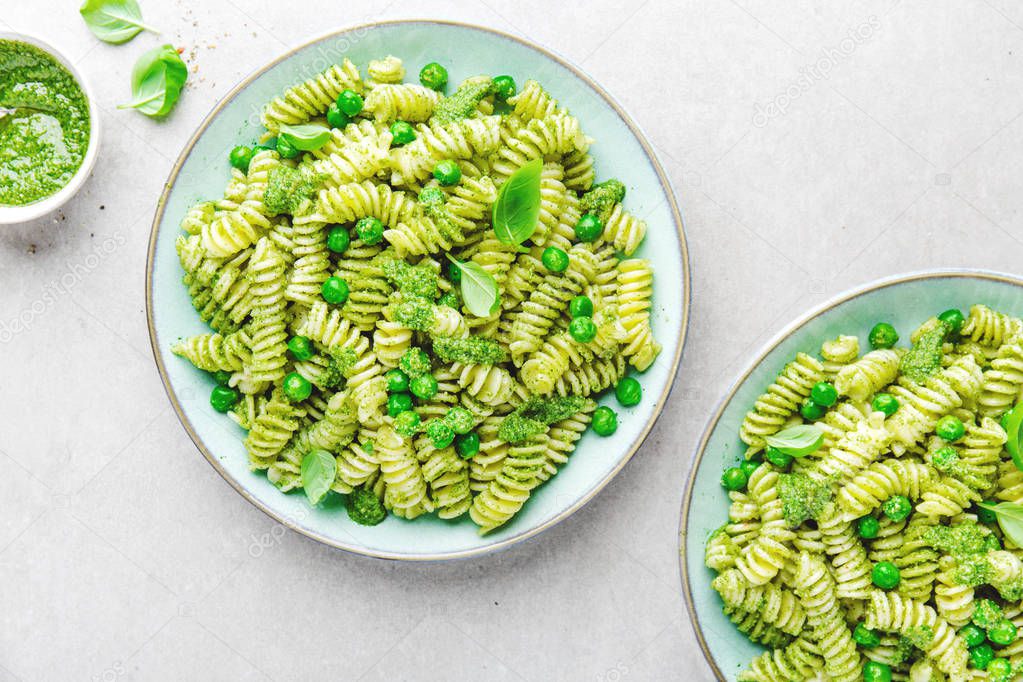 top view of italian pasta al bronzo with pesto sauce, green pea, basil and cheese served on grey tabletop