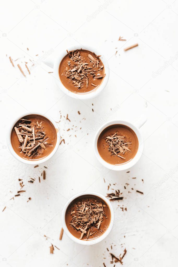 top view of hot chocolate with chocolate chunks and cream in small cups served on white background