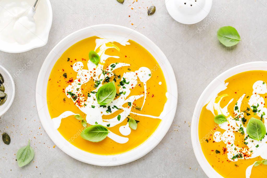 elevated view of Tasty appetizing pumpkin vegetable creamy soup decorated with basil, cream and spices on grey table