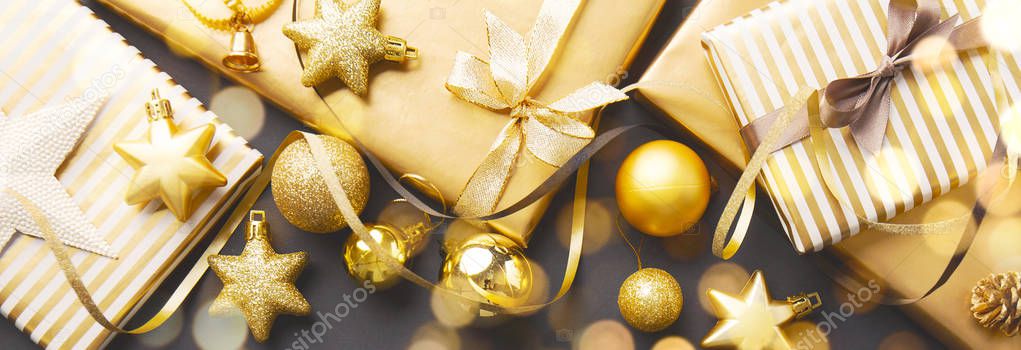 top view of beautiful christmas golden silver decorative baubles, gifts with shining lights and bokeh on dark black background