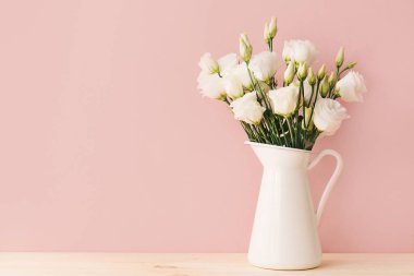 Yumuşak pembe bir arka plan üzerinde vintage vazoda beyaz çiçek açan gül