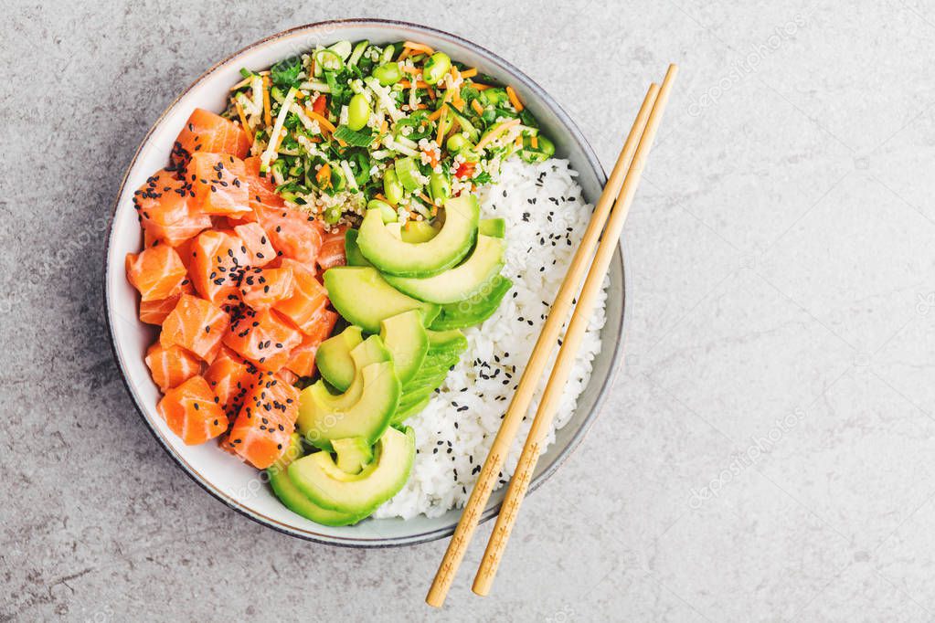 Tasty appetizing poke bowl with salmon, avocado, rice, salad with edamame on grey background