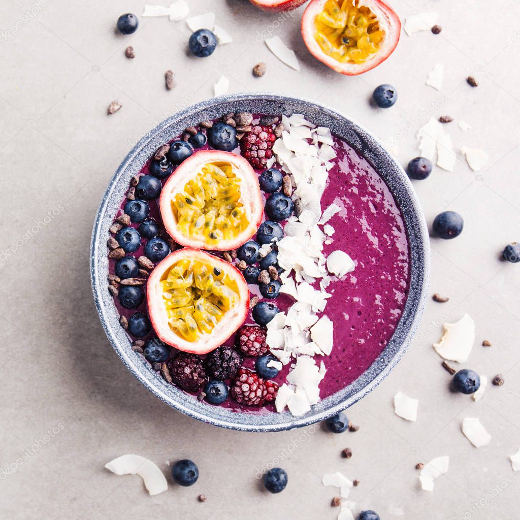 Tasty appetizing smoothie acai bowl made wild berries, decorated with cut passion fruit, coconut flakes, and cacao nibs on grey background