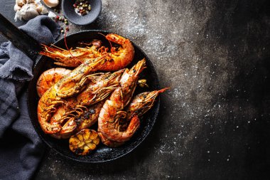 Koyu arkaplanda tavada servis edilen baharatlı ve sarımsaklı kızarmış karides.. 
