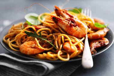 Karides ve domates soslu makarna koyu arkaplanda servis edilir.. 