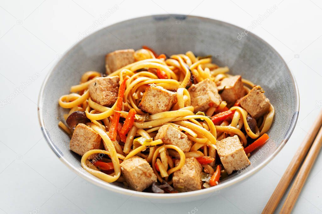 Tasty asian noodles with cheese tofu and vegetables on plates. 