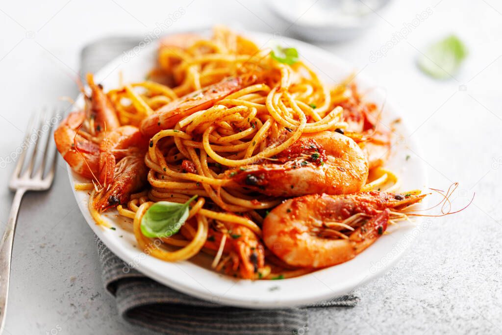 Pasta spaghetti with shrimps and tomato sauce served on plate on bright background. 