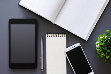 ofis çalışma tablo masası açılan Organizatör, boş not defteri, akıllı telefon, tablet, kalem ve yeşil saksılı bitki, koyu arka plan, üstten görünüm sahte