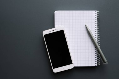 Boş beyaz defter kalem ve siyah ekran smartphone ile gri Ofis Masası üzerinde açıldı. Üstten Görünüm, kopya alanı.