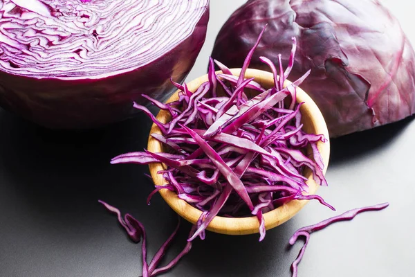 chopped red cabbage salad in wooden bowl with a half of cabbage head over dark gray background