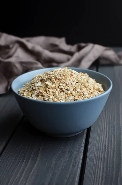 Rolled oats in ceramic bowl on dark wooden table with texture — Stock Photo, Image