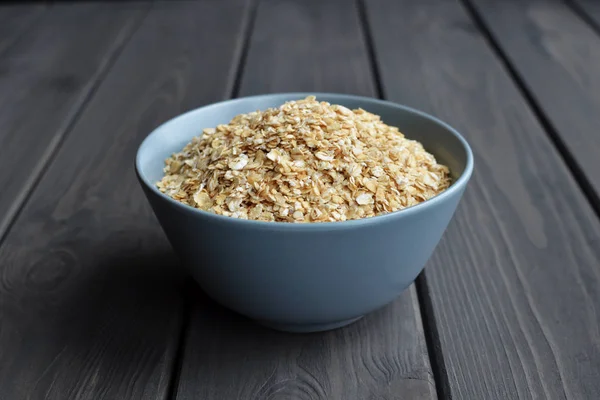 Rolled oats in ceramic bowl on dark wooden table background — Stock Photo, Image