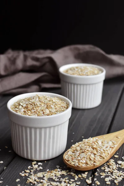Rolled oats in bowls and spoon on dark wooden table background