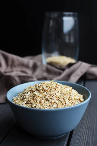 Rolled oats in ceramic bowl on dark wooden table with texture — Stock Photo, Image