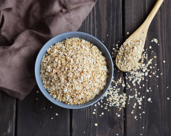 Rolled oats in bowl and spoon on dark wooden table, top view — Stock Photo, Image