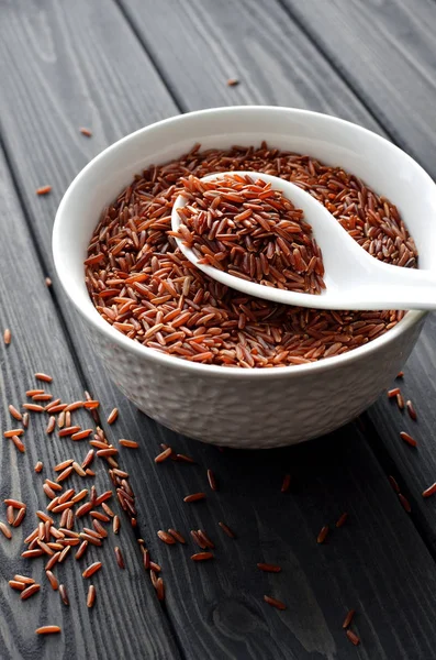 red rice in a ceramic bowl with spoon against dark wooden background