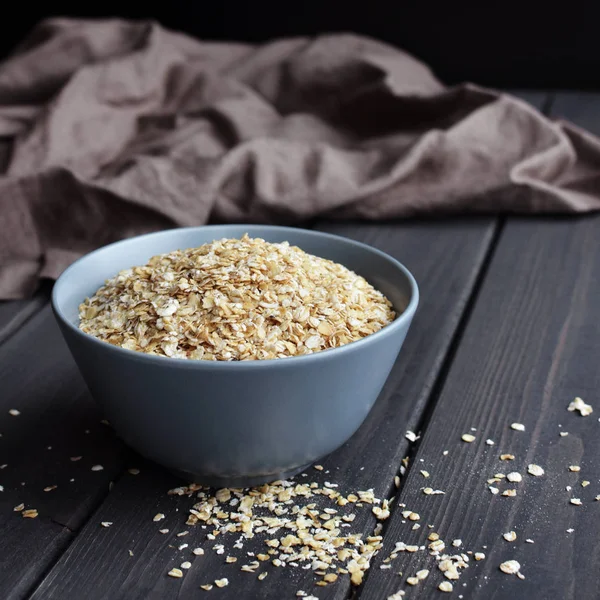 Rolled oats in ceramic bowl on dark wooden table with texture — Stock Photo, Image