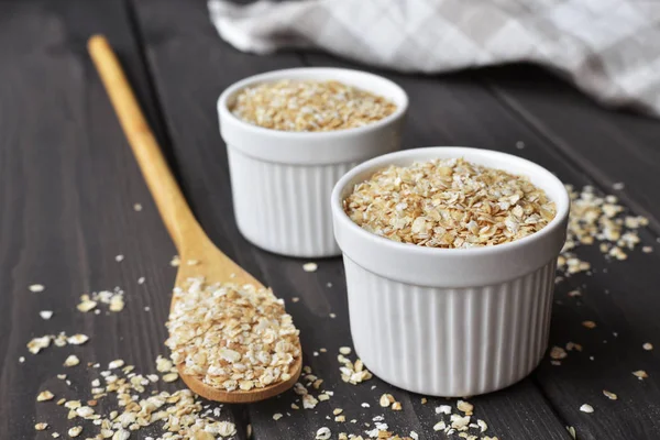 Rolled oats in bowls and spoon on dark wooden table background