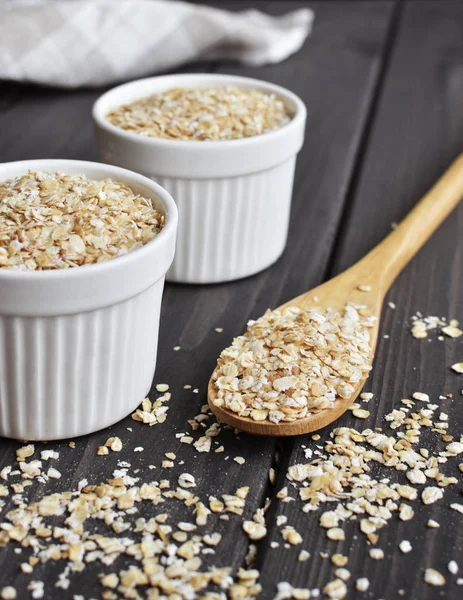 Rolled oats in bowls and spoon on dark wooden table background — Stock Photo, Image