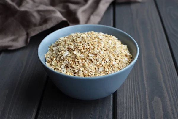 Rolled oats in ceramic bowl on dark wooden table with texture — Stock Photo, Image