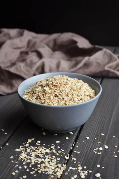 Rolled oats in ceramic bowl on dark wooden table with texture — Stock Photo, Image